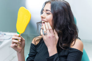 young female patient examining her smile in a handheld mirror